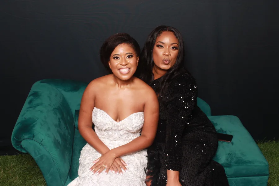 Two guests posed together on a green velvet couch at a formal event photo op