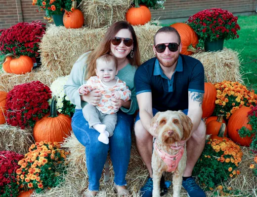 Family with a baby and dog photographed on hay bales among pumpkins at a fall photo op