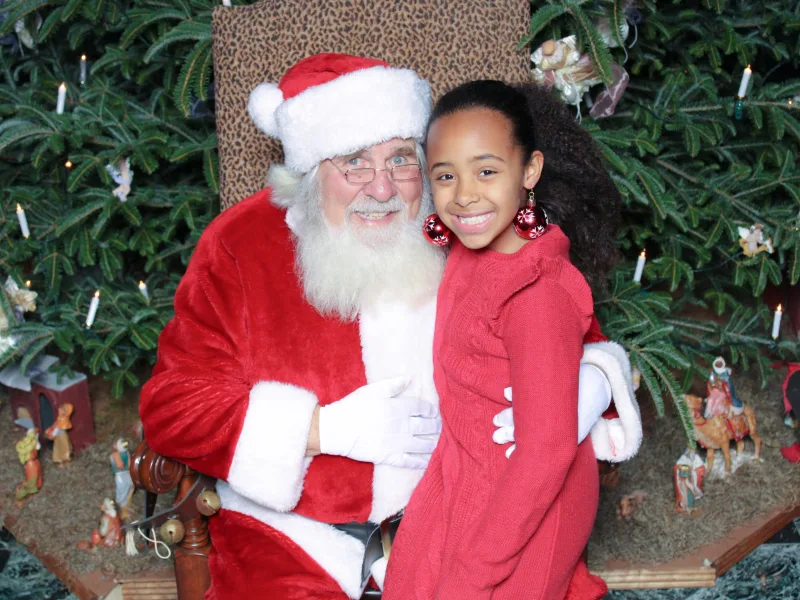 Child posing with Santa in front of a decorated Christmas tree at a holiday photo op