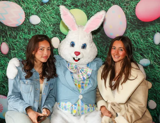 Two guests posing with the Easter Bunny in front of a pastel egg and grass backdrop