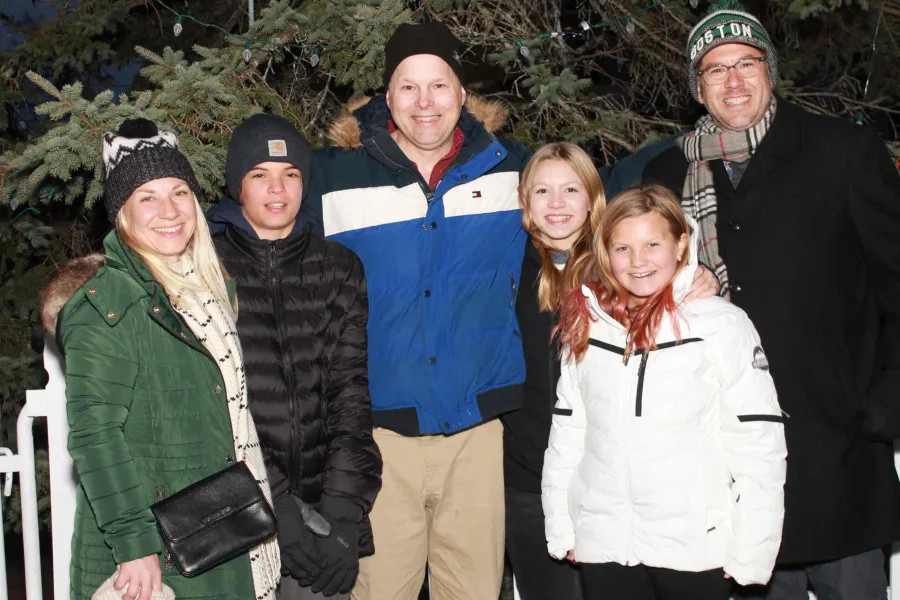 Family photographed outdoors at a town tree lighting with lit evergreens behind them