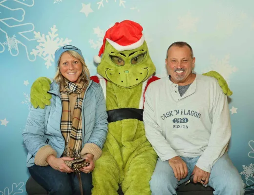 Couple posing with the Grinch at a holiday character photo op with a snowflake backdrop