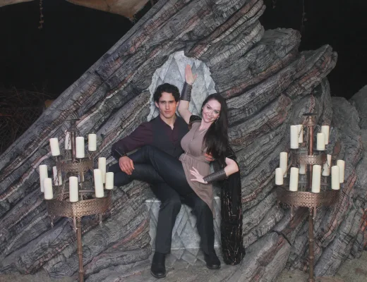 Couple posed on a dramatic themed set with candelabras and a sculpted rock backdrop