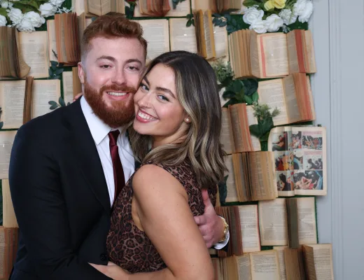 Couple photographed in front of a book page wall set with white florals