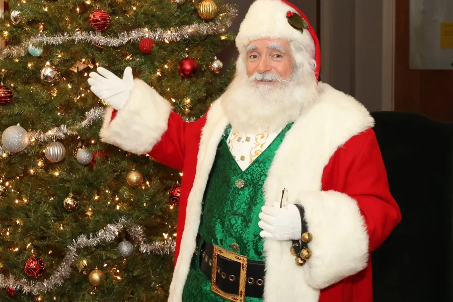 Santa gesturing beside a decorated Christmas tree at a holiday photo op station