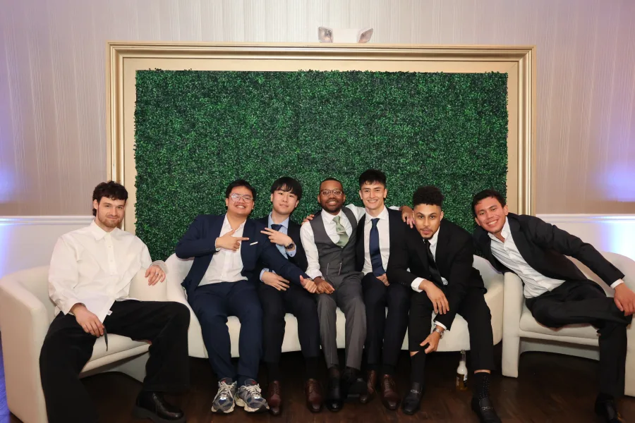 Group of guests photographed on a white sofa in front of a framed boxwood greenery wall