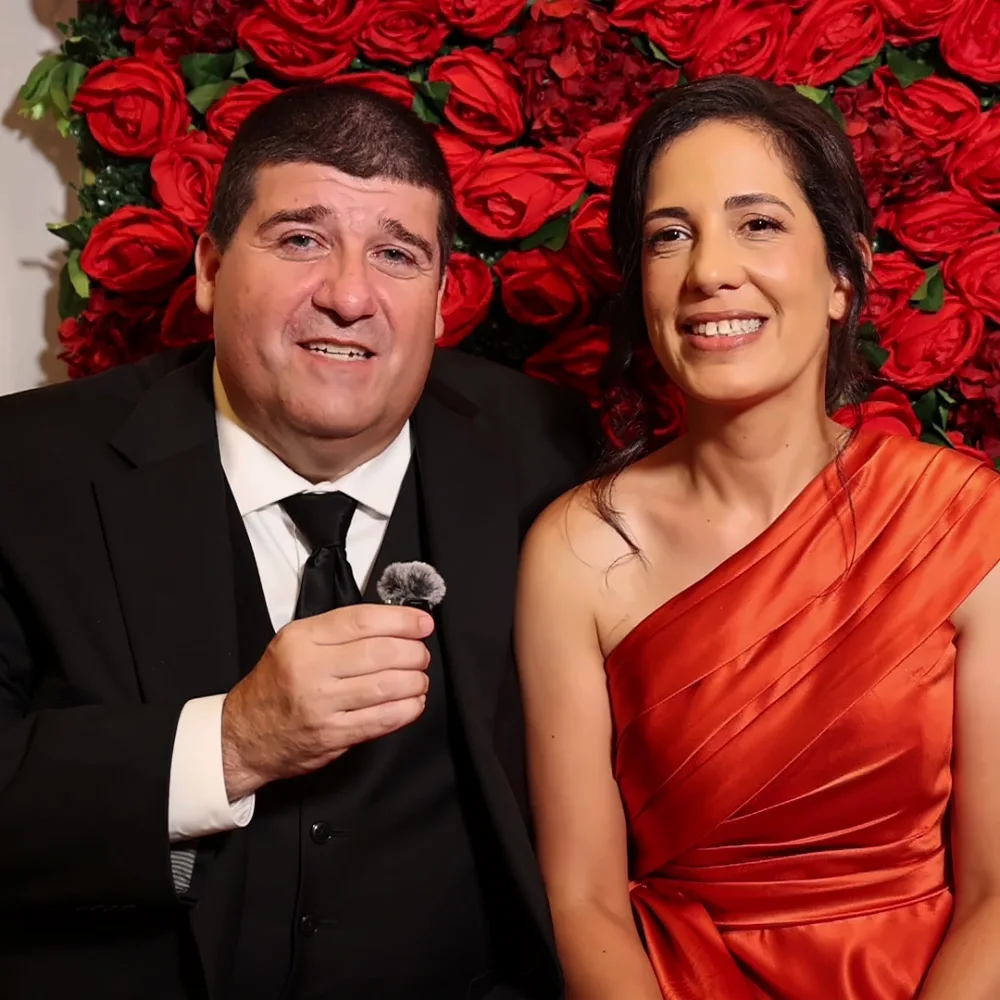 Couple smiling while recording a Confessional Booth message in front of a rose wall
