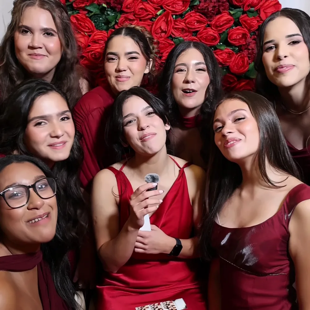 Group of friends laughing while recording a Confessional Booth message by a rose wall