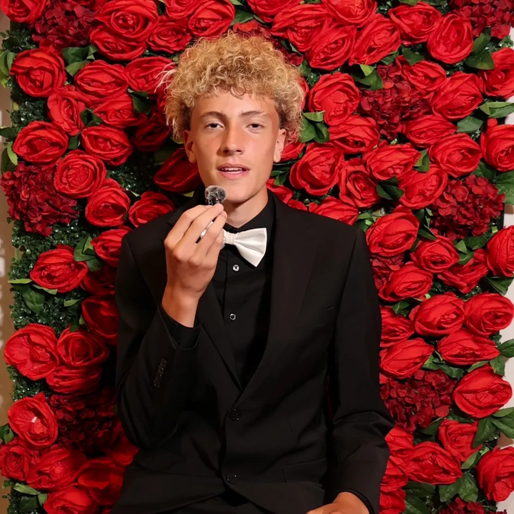 Young guest in a bow tie recording a Confessional Booth message by a rose wall