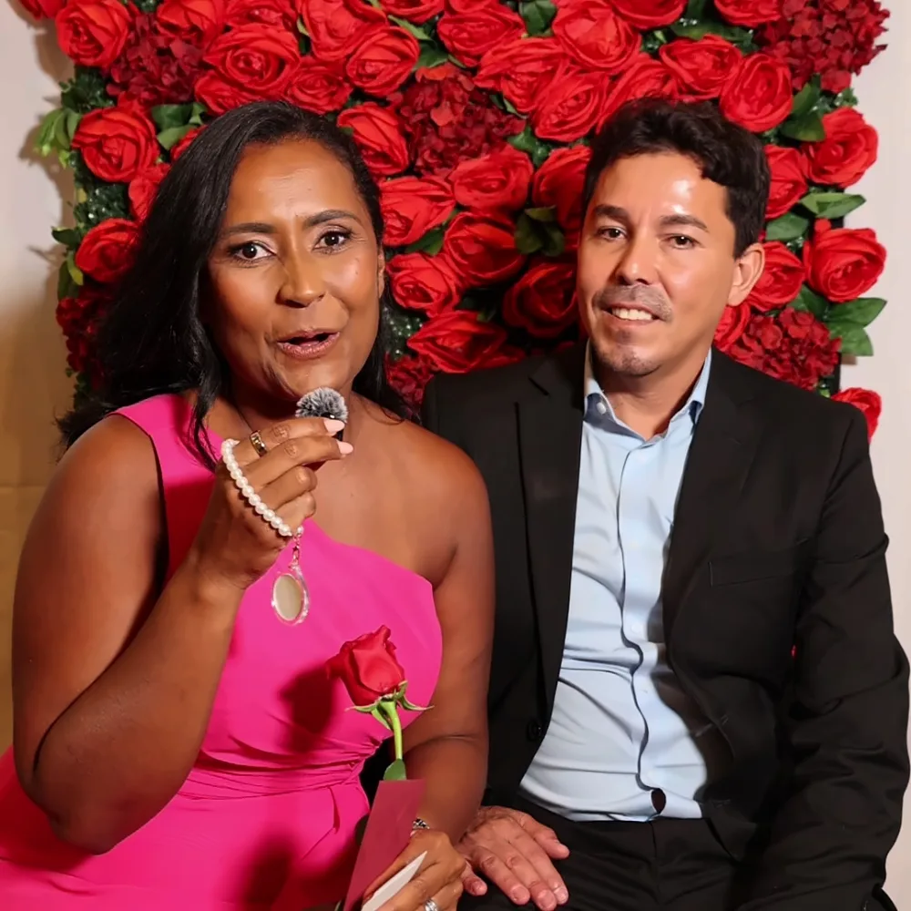 Couple recording a Confessional Booth video message in front of a rose wall